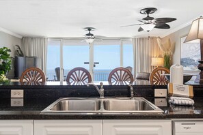 A modern kitchen with a large window, a ceiling fan, and a view of the ocean. - Oceanfront, 23rd floor Condo, Pools, Gym, Wifi (Panama City Beach)
