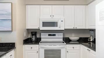 Una cocina con armarios blancos, microondas, estufa, cafetera y licuadora.
