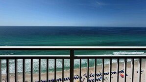 Blick auf den Strand vom Balkon aus, mit Geländer, Meer und badenden Gästen.