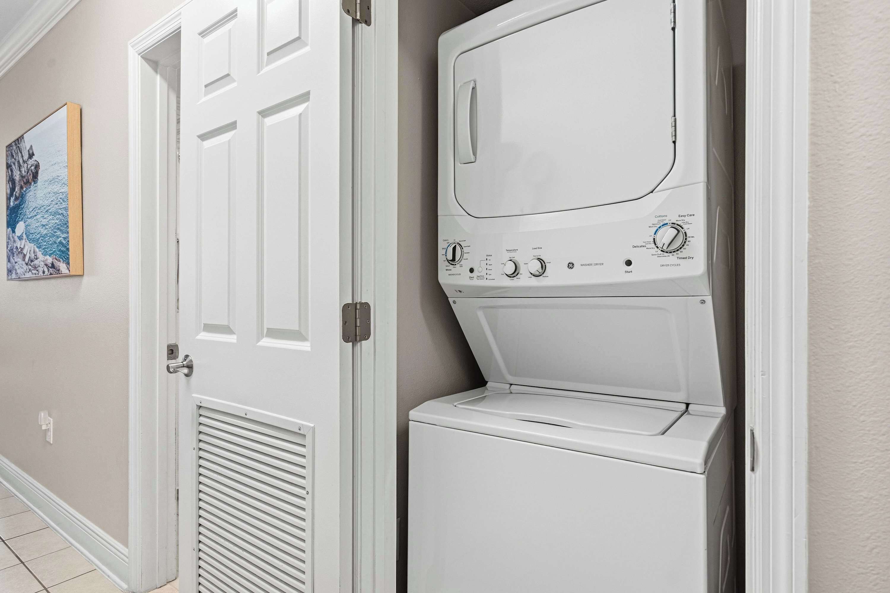 Une buanderie équipée d’un lave-linge et d’un sèche-linge à chargement frontal, d’une porte avec une poignée et d’une bouche d’aération fixée au mur.