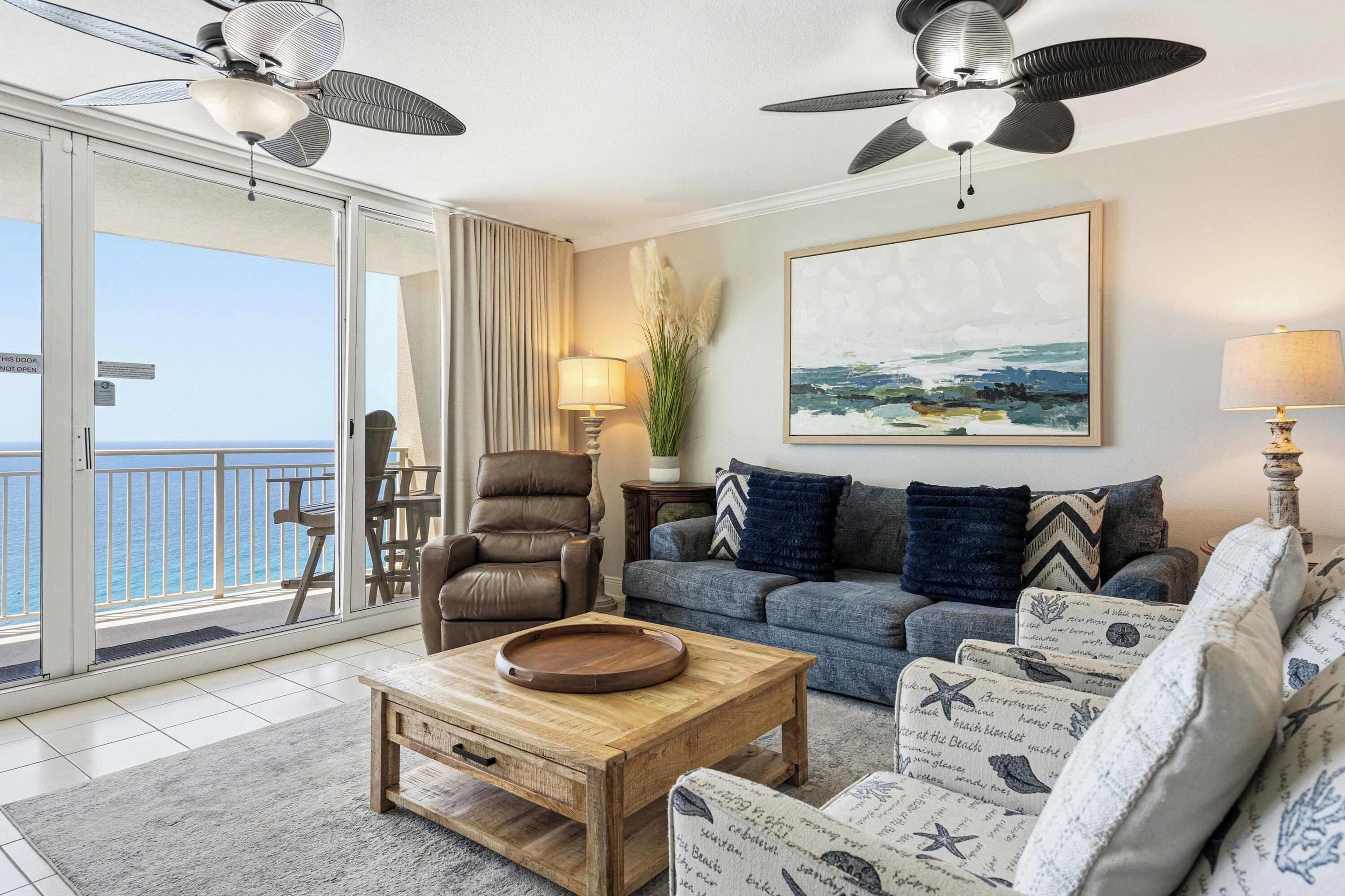 Ein geräumiges Wohnzimmer mit Balkon, Deckenventilator, einem Gemälde und Meerblick.