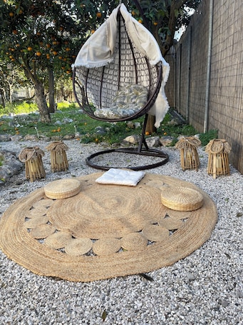 A garden area with a hanging chair, woven poufs, and a round woven mat.