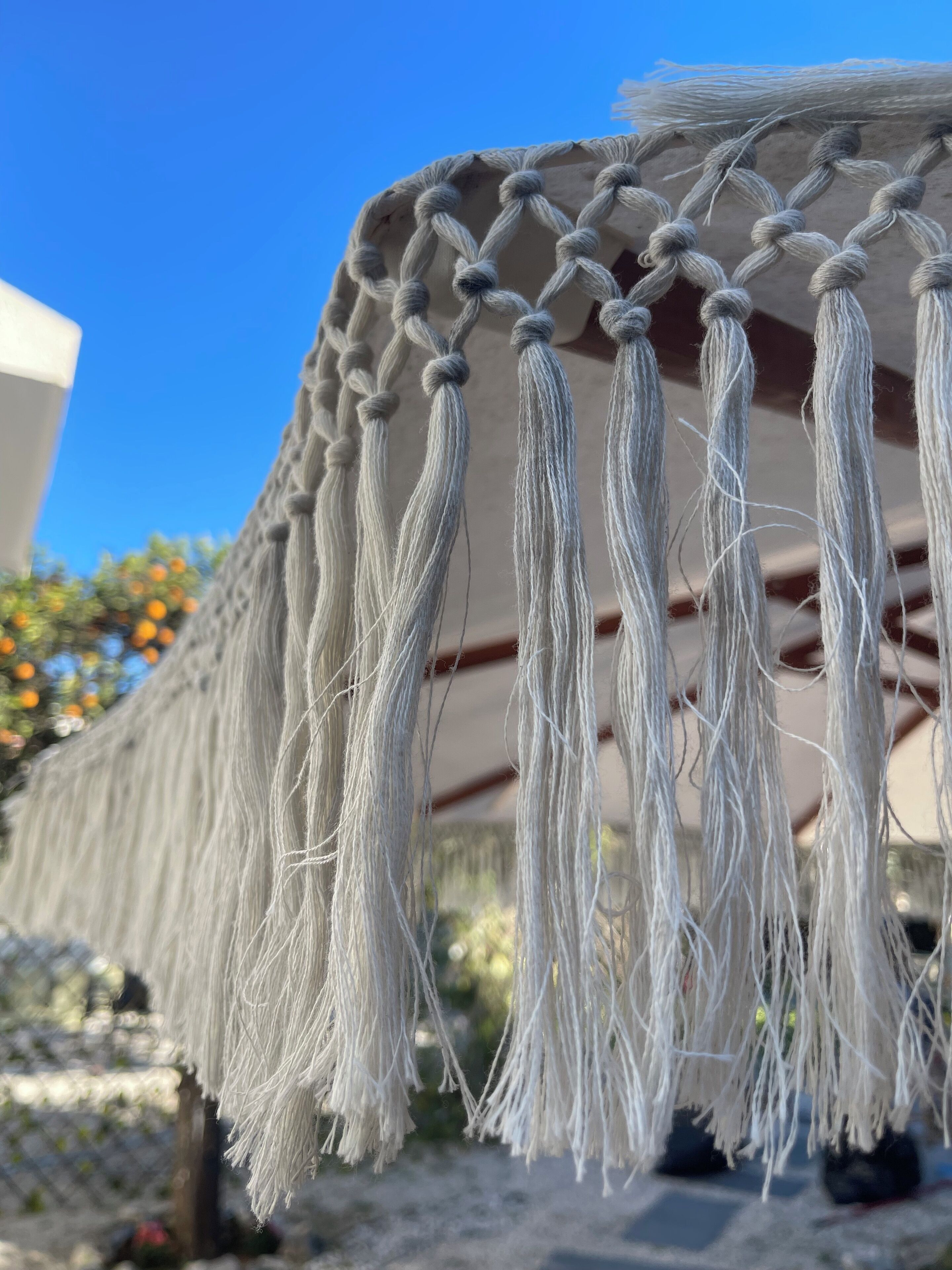 A macramé wall hanging with tassels, hanging from a ceiling.