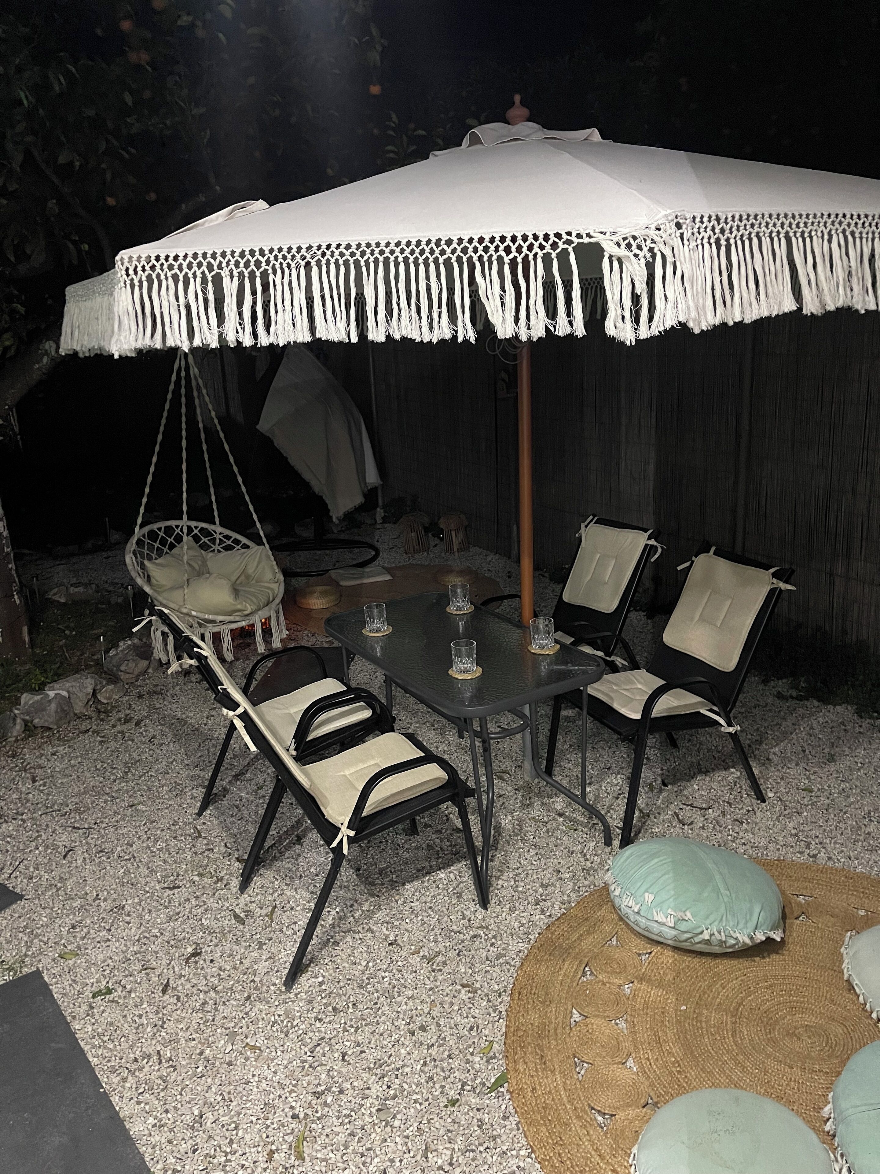 A covered outdoor seating area with a table and chairs, a hanging chair, and a woven floor mat.