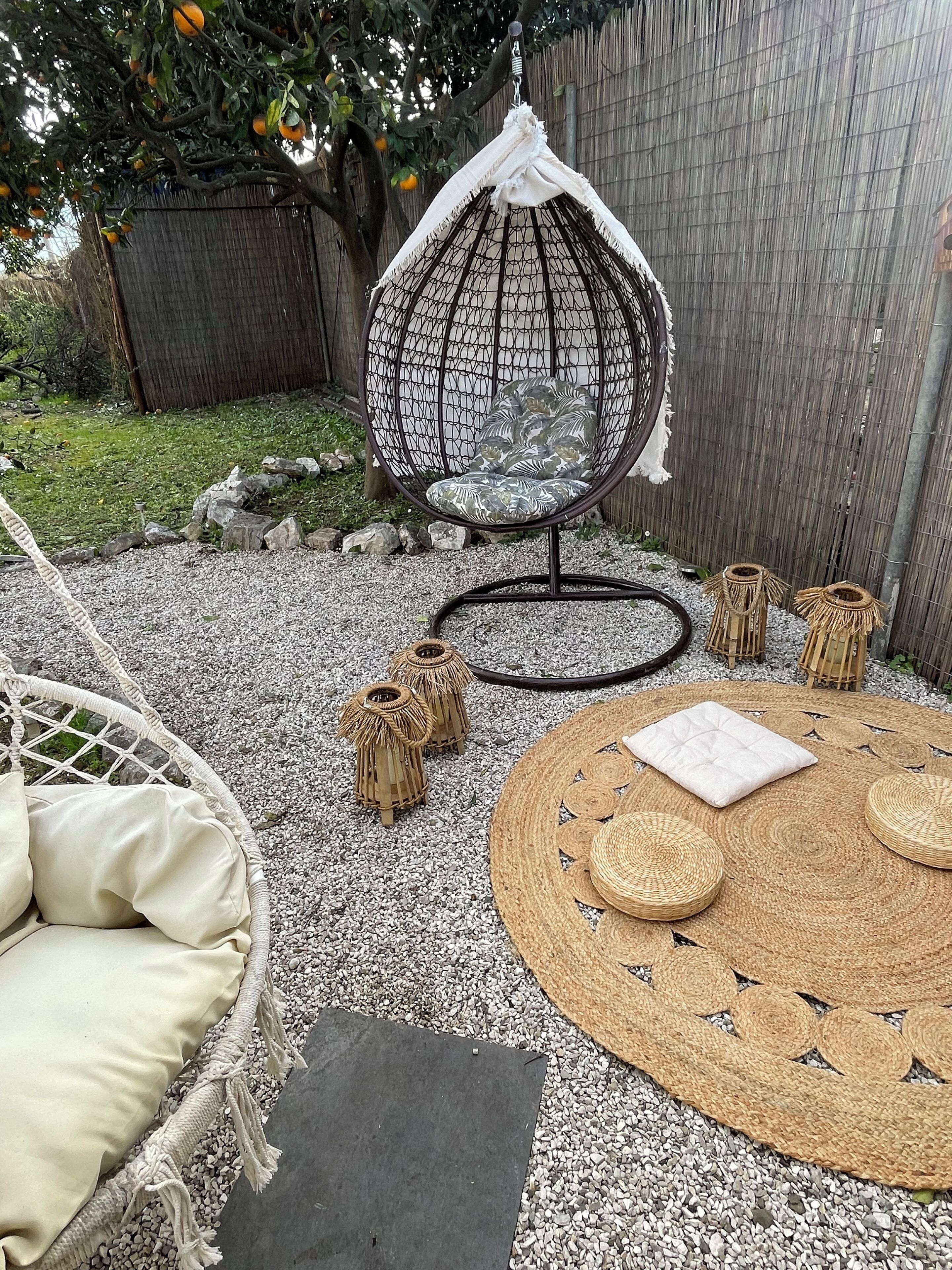 A garden area with a hanging chair, a round woven table, and two small lanterns.