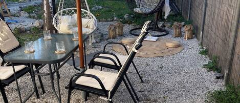 Eine Terrasse im Freien mit Tisch und Stühlen, einem Hängesessel und einem überdachten Bereich mit Makramee-Bordüre.