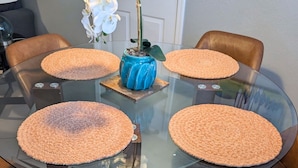 Un tavolo rotondo in vetro con quattro sottopiatti marroni, circondato da poltrone in pelle marrone.
