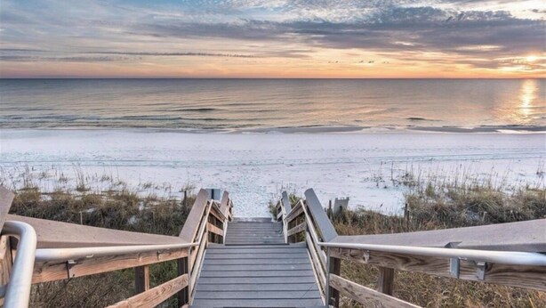 Une promenade en bois menant à une plage, avec un coucher de soleil en arrière-plan.