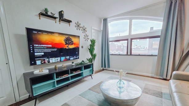 Ett vardagsrum med en platt-TV, ett soffbord, en soffa, ett fönster med gardiner och en växt.