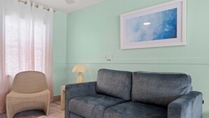 A room with a grey sofa, a wicker chair, a lamp, and a painting on the wall. - Handicap Accessible Suite in Clearwater Beach (Clearwater)
