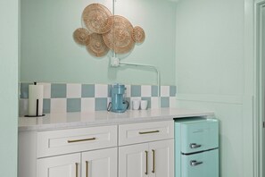 A kitchen with white cabinets, a teal refrigerator, a coffee maker, and a wall-mounted light fixture. - Handicap Accessible Suite in Clearwater Beach (Clearwater)