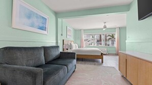 A bedroom with a grey sofa, a bed, a wooden cabinet, and a balcony with a railing. - Handicap Accessible Suite in Clearwater Beach (Clearwater)