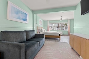 Een slaapkamer met een grijze bank, een bed, een houten kast en een balkon met een leuning.