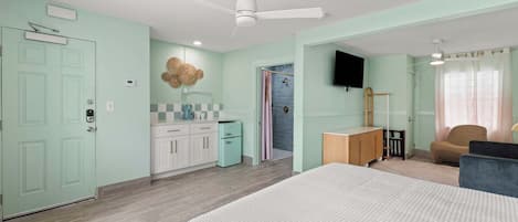 A bedroom with a bed, a desk, a chair, a television, and a shower.