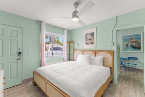 A bedroom with a bed, a ceiling fan, a window with a view of the street, and a painting on the wall. - The Bunk Room | Sparkling Pool, Steps to the Beach (Clearwater)