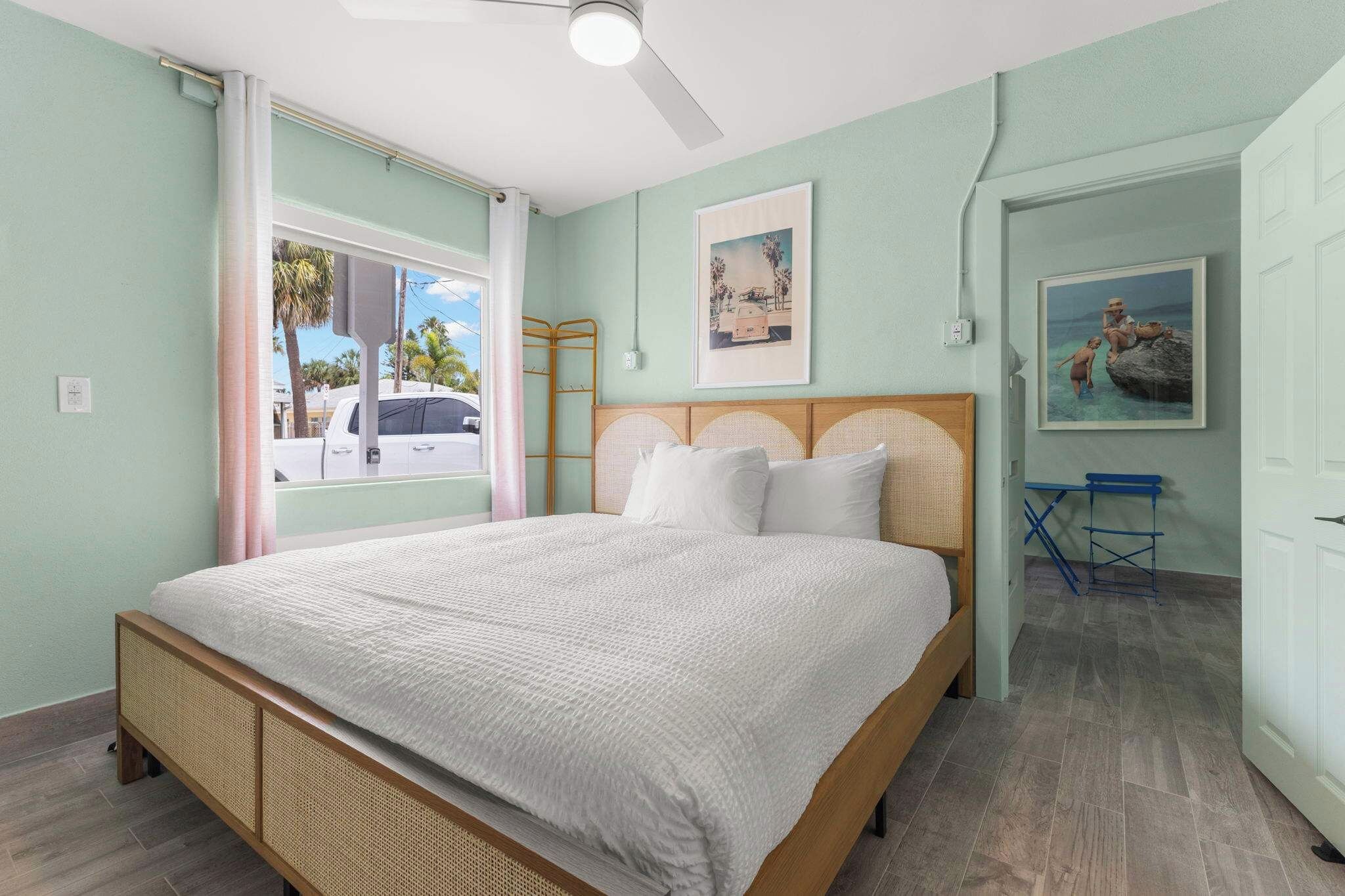 A bedroom with a bed, a window with a view of palm trees, and a door leading to another room.