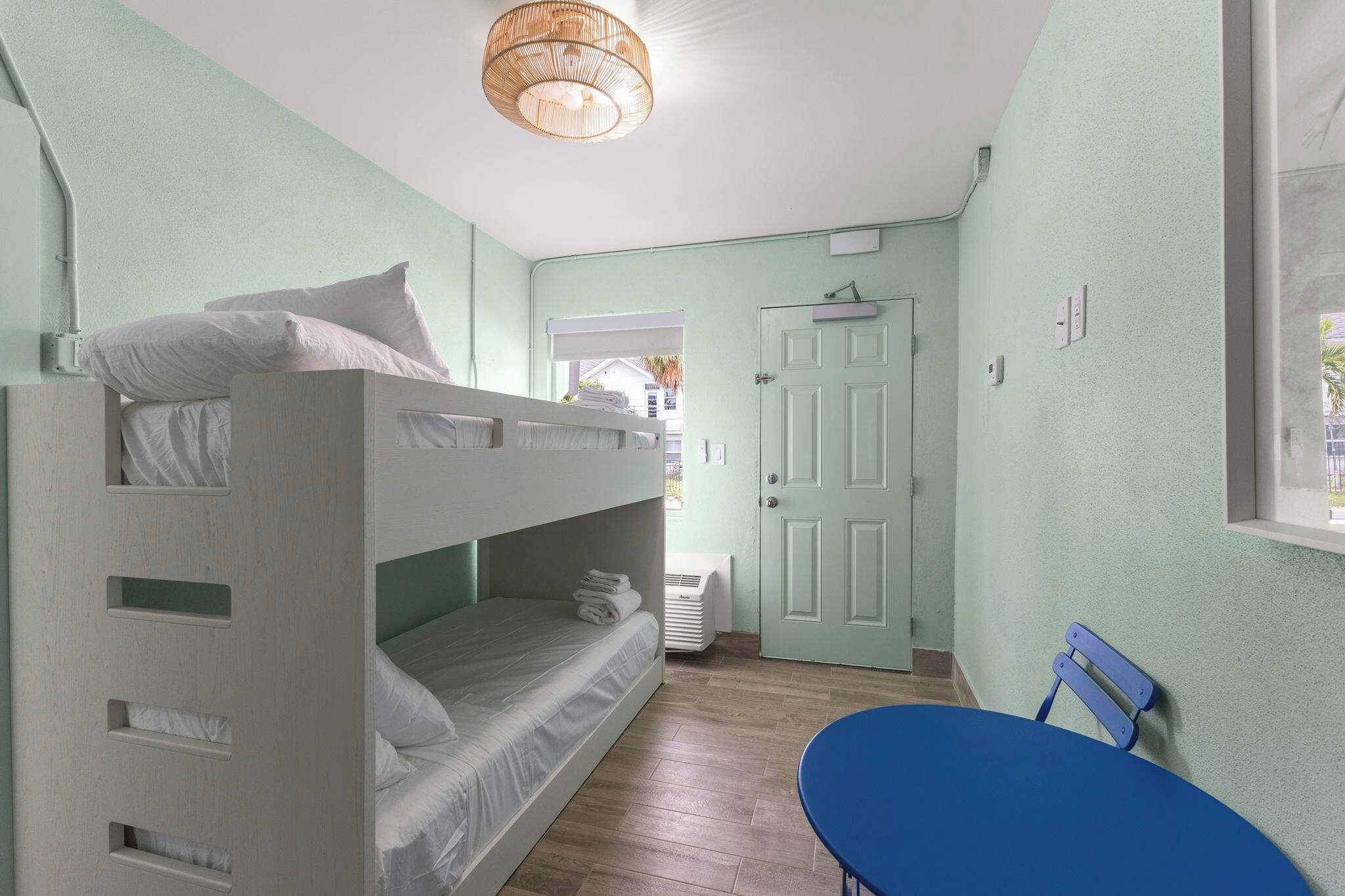 A room with bunk beds, a door, a window, and a blue chair.