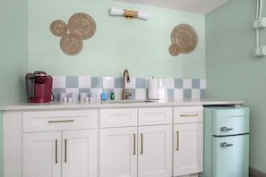 A kitchen with white cabinets, a red coffee maker, a sink with a gold faucet, and a vintage-style refrigerator. - The Bunk Room | Sparkling Pool, Steps to the Beach (Clearwater)