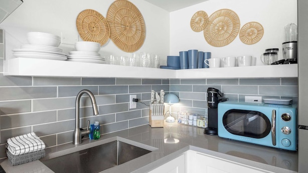Une cuisine moderne avec des carreaux gris, un évier, un micro-ondes bleu et des éléments décoratifs en forme d’œuvres d’art murales tissées.