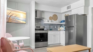 Une cuisine moderne avec des armoires blanches, un réfrigérateur en acier inoxydable, un four encastré et un coin repas comprenant une table et des chaises.