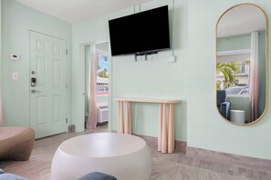 Een kamer met een wandgemonteerde flatscreen televisie, een ronde witte tafel, een klein console tafeltje en een spiegel met gouden lijst.