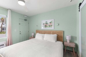 A bedroom with a bed, bedside tables, a headboard, a window with curtains, and a wall-mounted picture. - Coastal Suite - Sparkling Pool, Steps to the Beach (Clearwater)
