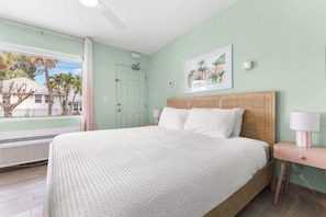 Une chambre à coucher avec un lit, une table de chevet, une lampe fixée au mur et une fenêtre avec des rideaux.