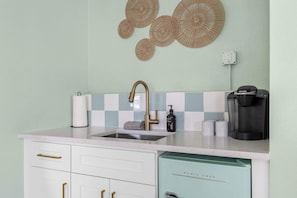 Une cuisine équipée d’un évier, d’un robinet, d’une machine à café et agrémentée d’œuvres d’art décoratives sur les murs.
