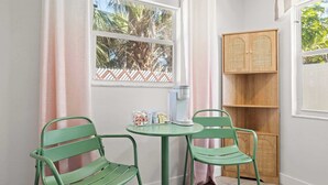 Een kamer met een raam, twee groene stoelen, een klein tafeltje, een koffiezetapparaat en een houten kast.