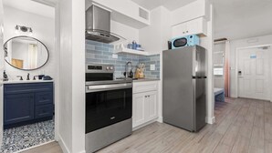 Een moderne keuken met een roestvrijstalen koelkast, oven en magnetron, witte kastjes en een blauwe spatwand.
