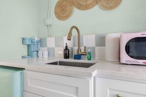 Una cocina con un lavamanos de acero inoxidable, una cafetera y un microondas.