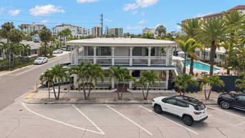 A two-story building with a balcony, surrounded by palm trees and a parking lot.