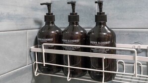 Drie flessen 'Grown Alchemist' producten staan op een wit schap voor een betegelde muur.