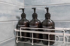 Tres botellas de productos 'Grown Alchemist' sobre una estantería blanca frente a una pared con azulejos.