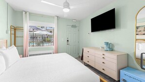 Een hotelkamer met een bed, een dressoir, een televisie en een raam met uitzicht op een zwembad en gebouwen.