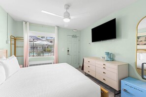Habitación de hotel con cama, cómoda, televisor y ventana con vistas a una piscina y edificios.
