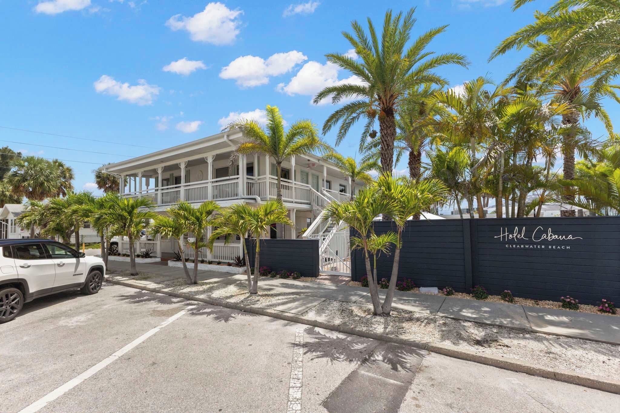 A two-story hotel with a white facade, a covered porch, and a black fence with the hotel's name.