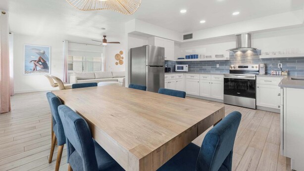 Een moderne keuken met witte kasten, roestvrijstalen apparatuur en een eethoek met een houten tafel en blauwe stoelen.