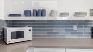 Een keuken met een magnetron, een wit aanrecht en een betegelde spatwand.