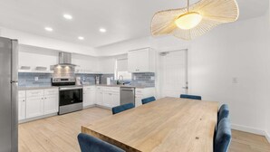 Een moderne keuken met witte kasten, een houten eettafel en blauwe stoelen.