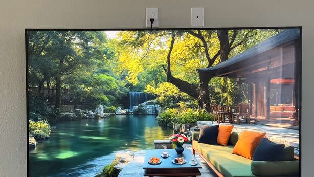 A television displaying a serene garden scene with a pond, waterfall, and outdoor seating area.