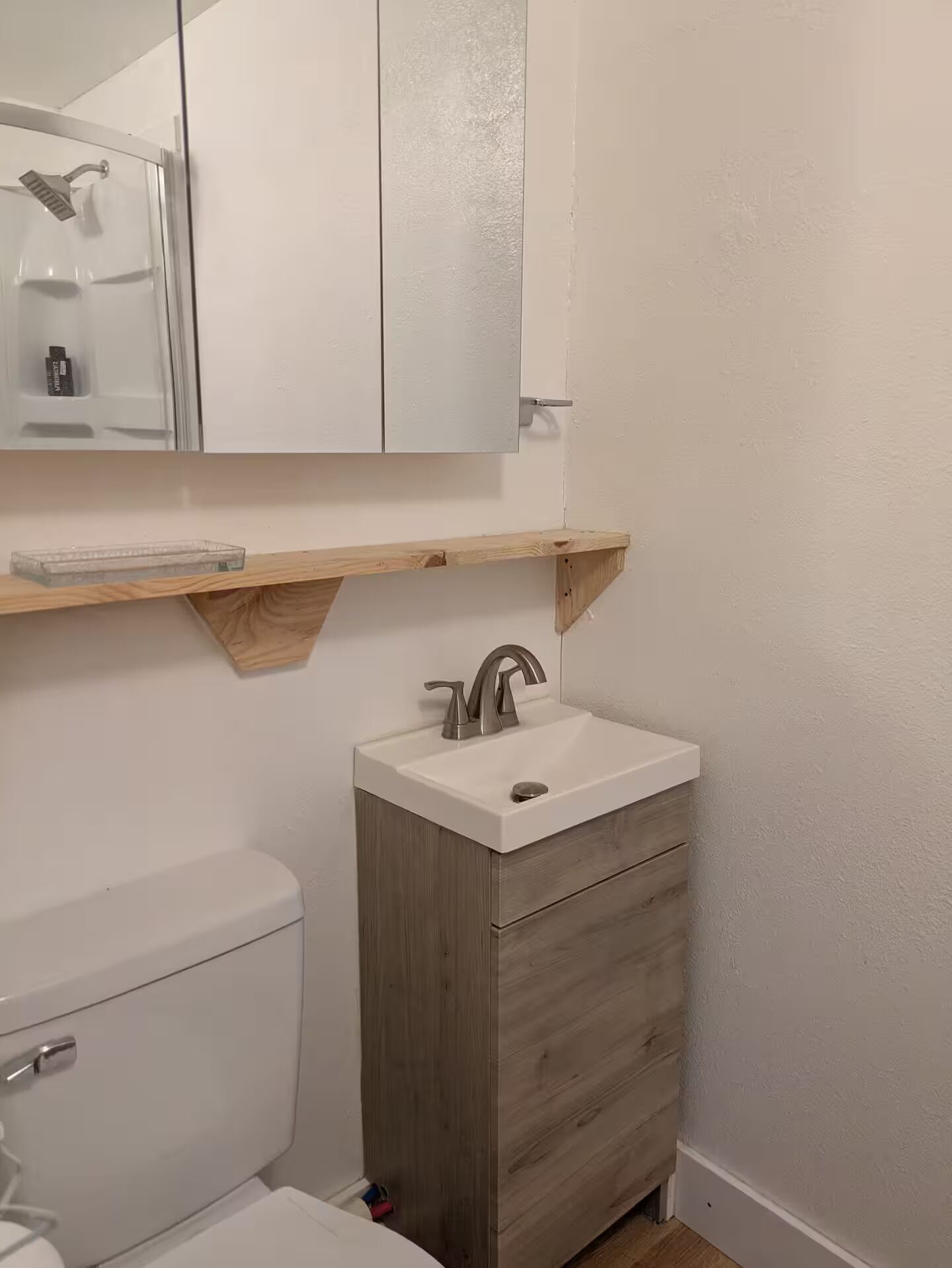 Une salle de bain comprenant des toilettes, un lavabo avec un meuble en bois, un miroir et une douche.