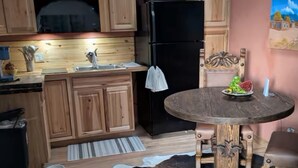 Una cocina con armarios de madera, un refrigerador negro, una mesa de comedor con alfombra de cuero de vaca y un ventilador de techo.