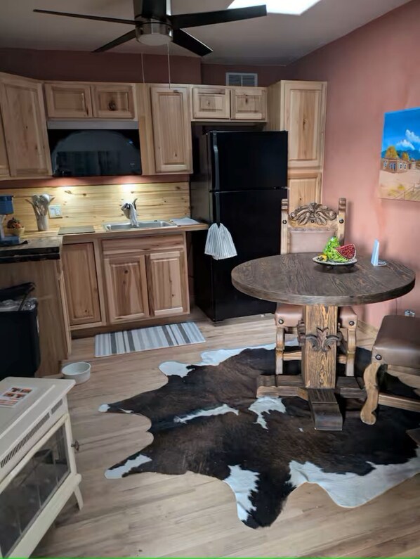 A kitchen with wooden cabinets, a black refrigerator, a dining table with a cowhide rug, and a ceiling fan.