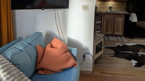 Una sala de estar con un sofá azul, un televisor montado en la pared y un arco que da a una zona de cocina.