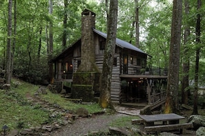 Un chalet rustique doté d’une cheminée en pierre, d’une terrasse en bois et d’un sentier en pierre menant à l’entrée.