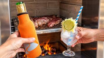 A person holding a bottle and a drink with a straw in front of a grill.