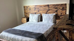 A bedroom with a wooden headboard, a bed with patterned bedding, a nightstand, a desk with a chair, and a ceiling fan. - Home away from home (Palacios)