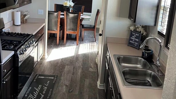 A compact kitchen with dark cabinetry, a gas stove, a sink, and a dining area with a table and chairs. - Home away from home (Palacios)