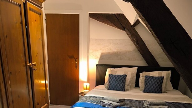 A bedroom with a bed, wooden wardrobe, and a sloped ceiling.